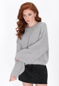Grauer, flauschiger Pullover mit übergroßen Ärmeln und rundem Halsausschnitt, kombiniert mit einem schwarzen Jeansrock. Weicher, strukturierten Stoff durchgehend.