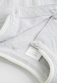 Helles graues Babybekleidungsstück mit strukturiertem Muster und gestreiftem Kragen. Verfügt über weiße Knopfverschlüsse und ein Pflegeetikett, das innen sichtbar ist.