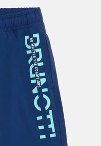 Calções atléticos azul-marinho com cintura elástica, apresentando um texto audacioso em azul-claro "BRUNOTTI" e a frase "NÃO IMPORTA AS CONDIÇÕES."