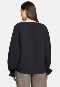 Zwarte blouse met lange mouwen gemaakt van lichtgewicht stof. Heeft een brede halslijn, elastische manchetten en een ontspannen pasvorm. Minimalistisch ontwerp.