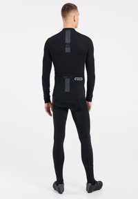Maillot de cyclisme noir à manches longues avec un design ajusté, présentant des stripes réfléchissantes verticales dans le dos, et une poche arrière zippée.