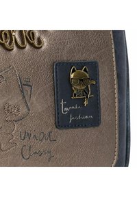 Bronzefarbenes Texturen-Tasche mit dunkelblauen Akzenten; verfügt über eine goldene Katzennadel mit Brille und geprägt Text, das "Einzigartig Elegant" liest.