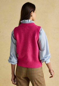 Roosa kootud vest ribiga ä�ärega, kantud helesinise volangkraega särgi ja mustriliste pruunide pükste peal, vaadatuna selja tagant.