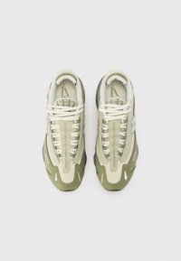 Zapatillas deportivas con una parte superior de malla en crema y verde oliva, que presentan un diseño de cordones, un collar acolchado y una suela exterior de goma negra.