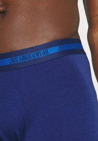 Mutande da uomo blu navy con una texture liscia e una cintura elastica blu a contrasto con la scritta "JBS UNDERWEAR" stampata.