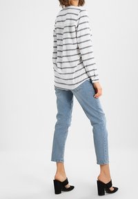 Gestreiftes Langarmhemd in Weiß und Marineblau, kombiniert mit hellblauen Jeans. Schwarze hohe Sandalen mit strukturiertem Obermaterial.