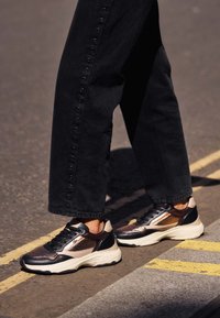 Sneakers o podwójnej tonacji z czarnymi, beżowymi i metalicznymi akcentami. Cholewka ma teksturę z meszu i skóry, z grubą białą podeszwą.