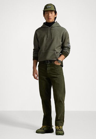 Sudadera verde oliva con bolsillo canguro, combinada con pantalones verde oscuro y zapatillas verdes. Incluye una gorra y un reloj a juego.