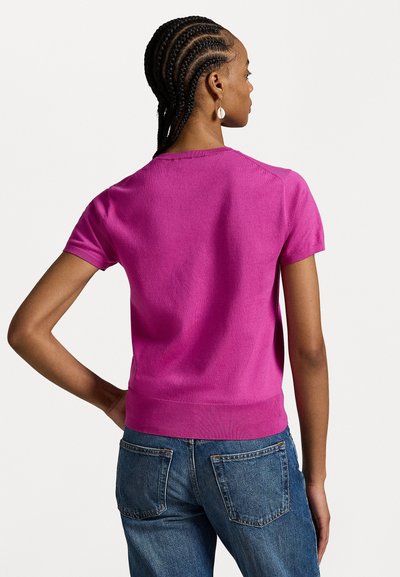 Pull rose à manches courtes, ajusté, avec une texture lisse et des poignets côtelés, associé à un jean en denim bleu avec des poches arrière.