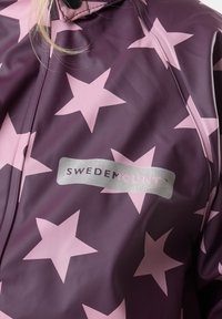 Bordeauxregenjas met grote roze sterpatronen, met een zilveren "SWEDEMOUNT"-logo. Gemaakt van waterdicht materiaal met een soepele textuur.