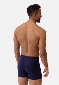 Gli slip boxers blu navy presentano un design aderente con un elastico rosso in vita. Il tessuto sembra morbido con una texture liscia.