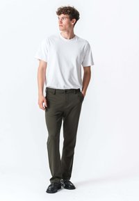 Hvid kortærmet t-shirt parret med olivengrønne bukser. Bukserne har knaplukning og sidelommer. Modellen står i en neutral pose.