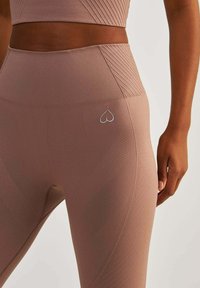 Dopasowane, wysokie legginsy w miękkim, jasnoróżowym materiale. Posiadają teksturalne wzory i małe logo w kształcie serca na biodrze. Bezszwowy design.