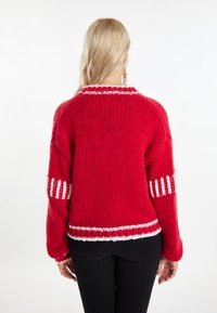 Piros kötött pulóver laza fazonban, fehér csíkokkal az ujjakon és az alján, valamint magas gallérral. Az egész felületét textúrált minta díszíti.