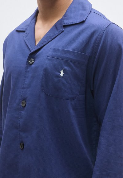 Μπλε ναυτικό παντελόνι πιτζάμας από απαλό, υφασμάτινο ύφασμα με υφή. Διαθέτει μία τσέπη στο στήθος με κεντημένο λογότυπο και μαύρα κουμπιά.