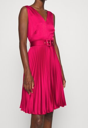Vestido fucsia sin mangas con escote en V, cinturón ajustado en la cintura y falda plisada hasta la rodilla en una persona de pie.
