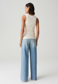 Top senza maniche beige chiaro abbinato a jeans blu sbiaditi a gamba larga. Il top presenta un collo rotondo, mentre i jeans hanno un design classico a cinque tasche.