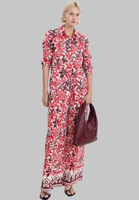 Bloemenpatroon, knoop-up jurk in rood en room; heeft lange mouwen en een gestrikte taille. Inclusief een textuurburgundy handtas.