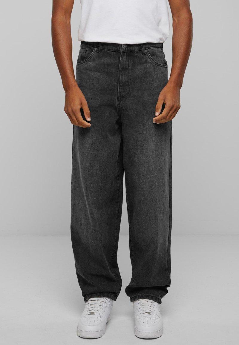 Black high-waisted denim jeans with a relaxed fit, featuring five pockets and a button closure, paired with white sneakers.