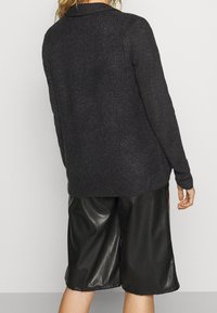 Mörkgrå stickad tröja med avslappnad passform och textilstruktur, parat med svarta blanka lädershorts, sedd bakifrån.