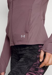 Fitted purple zip-up jacket with ribbed texture and pockets, paired with black leggings featuring a pink abstract pattern and reinforced seams.