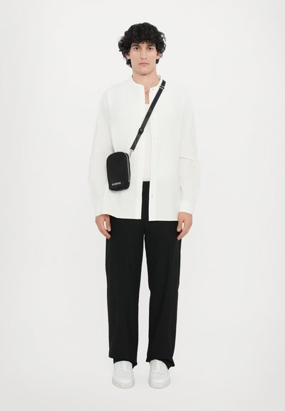 White long-sleeve button-up shirt, black loose trousers, and white sneakers. Black crossbody bag with zipper, worn across the shoulder.