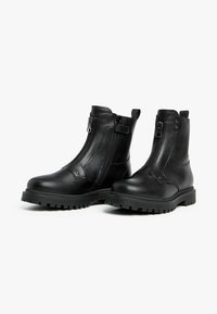 Black leather ankle boots with two side zippers, chunky rubber sole, and a smooth texture. Features pull tabs for easy wear.