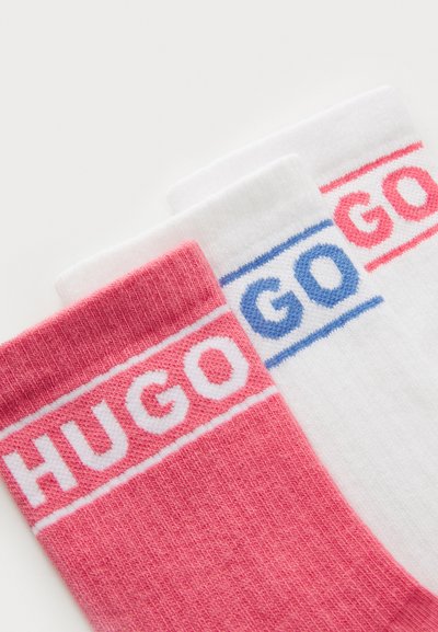 Trois paires de chaussettes de type « crew » : une rose, une blanche et une avec du bleu clair. Chacune arbore « HUGO » en lettres grasses sur les bandes.