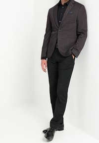 Blazer corto a fantasia scura con due tasche frontali, abbinato a una camicia nera e pantaloni. Scarpe nere completano l'aspetto formale.