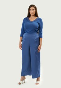 Top blu con scollatura in pizzo, maniche 3/4, abbinato a pantaloni blu a gamba larga in tessuto morbido. Indossato con sandali con tacco bianchi.