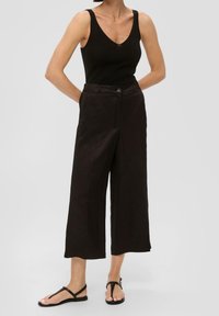 Černé široké kalhoty vyrobené z lehkého materiálu s hladkou texturou, s knoflíkovým zapínáním a bočními kapsami, spárované s přiléhavým černým topem bez rukávů.