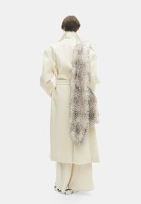 Crème-kleurige, oversized coat met een hoge kraag, voorzien van een gestructureerde, vachtachtige schouderaccent. Glad stof met wijde mouwen en een riem.