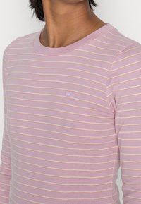 Maglietta a maniche lunghe rosa chiaro con strisce orizzontali color crema e scollatura tonda. Presenta un piccolo logo Levi's sul petto. Tessuto dalla consistenza liscia.