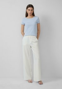 Haut court à manches courtes bleu clair à côtes avec des poignets festonnés, associé à un pantalon large rayé blanc, et des sandales argentées à lanières.