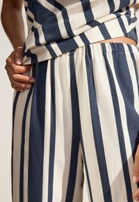Striped cotton pants featuring navy and cream vertical stripes, with an elastic waistband and a lightweight, textured fabric.