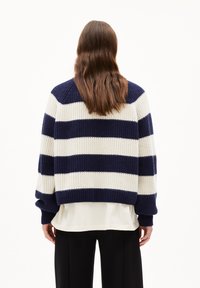 Pull en tricot avec des rayures horizontales bleu marine et crème, coupe oversize, texture côtelée et épaules tombantes. Porté par-dessus un haut léger.