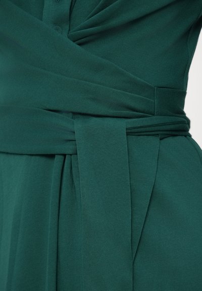 Πράσινο φόρεμα από ύφασμα με σχεδιασμό τύπου wrap, που διαθέτει ζώνη για δέσιμο, απαλό ύφασμα και διακριτικές λεπτομέρειες στην εφαρμογή στη μέση.