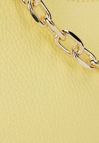 Gelbes Leder mit einer strukturierten Oberfläche, verziert mit einer goldenen Metallkette als Akzent, hebt eine harmonische Farbkombination hervor.