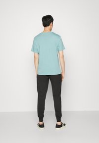 Ljusblå kortärmad t-shirt kombinerad med svarta joggingbyxor. T-shirten har en rund halsringning, medan byxor har en tapered passform och muddar.