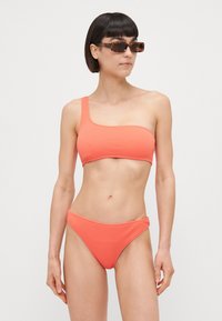 Set bikini corallo con top a spalla unica e slip classico, realizzato in tessuto testurizzato con una finitura liscia.