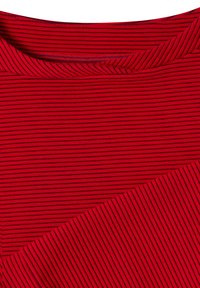 Gros plan d’un tissu rouge avec de fines rayures horizontales noires et un coin plié montrant les détails de la texture et du motif.