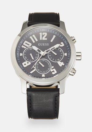 Montre avec bracelet en cuir noir, affichant un cadran gris avec de grands chiffres blancs, trois sous-cadrans et des accents en ton argenté. Boîtier en acier inoxydable.