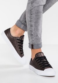 Baskets en mesh noir avec semelles en caoutchouc blanches, ornées d'accents métalliques texturés, lacets noirs et design à bout rond.