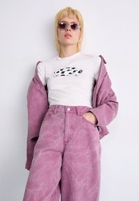 Veste en denim rose et jeans taille haute assortis, accompagnés d'un t-shirt blanc avec un motif de vache en noir et blanc.