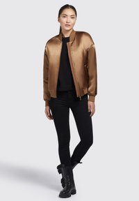 Satin bomberjack in bruin, met een ritssluiting aan de voorkant, geribbelde kraag en manchetten, gecombineerd met zwarte skinny jeans en zwarte enkellaarsjes.