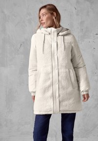Witte winterjas met een pluche fleece voorkant, gladde nylon mouwen en een capuchon. Beschikt over geribbelde details, drukknoopjes en zijzakken.