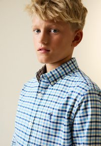 Blau-weiß kariertes Hemd mit kontrastierendem Button-Down-Kragen in Braun und Blau. Verfügt über ein kleines, gesticktes Hummer-Logo auf der Brust.