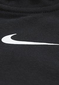 Tela negra con una textura suave que presenta un destacado logo blanco de Nike en un diseño curvado, colocado en diagonal sobre el material.
