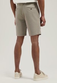 Gyeplőtől látható, egyenes szabású khaki rövidnadrág, pamutból készült, hátul gombos zsebekkel, világos sneaker cipővel párosítva.