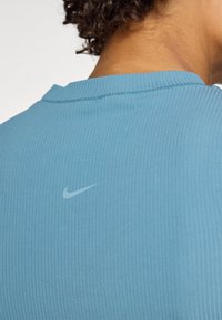 Heledad helesinise ribaga särk ümmarguse kaelusega. Seljal on väike, tagasihoidlik Nike logo veidi tumedamas toonas.